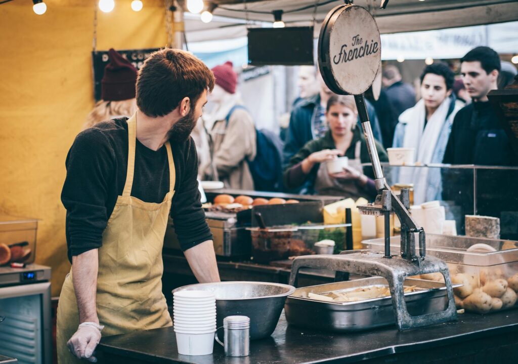 Man cooking at busy outdoor food market stall.