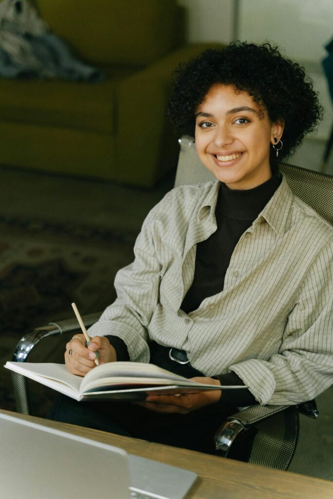 Woman smiling, writing in notebook at desk.