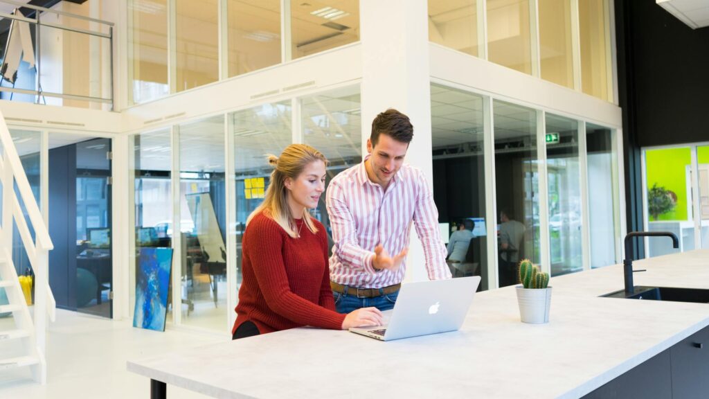 Colleagues collaborating at office standing desk with laptop.