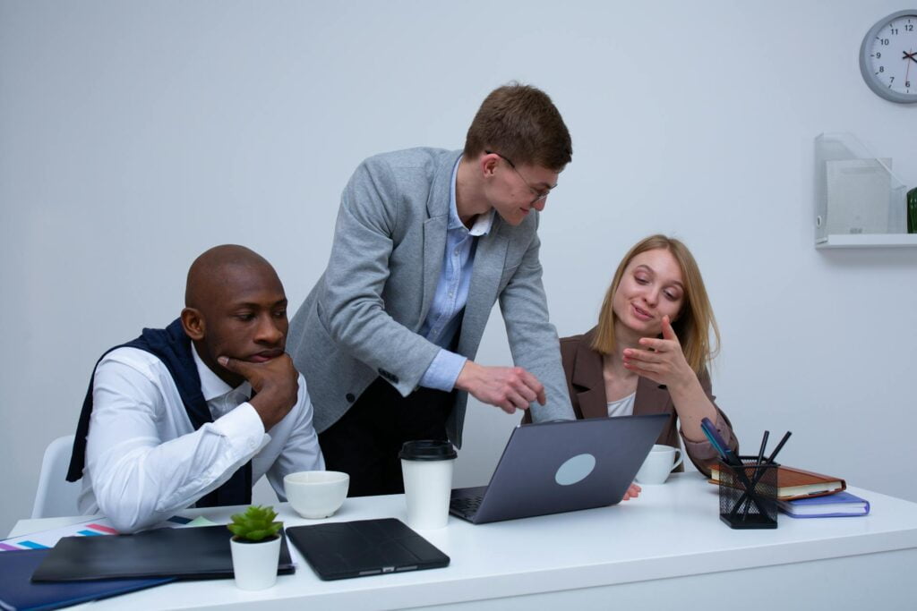 Three colleagues discussing work on laptop in office.