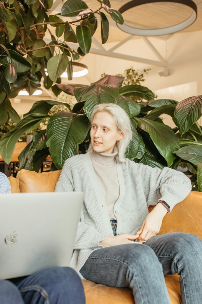 Woman working on laptop in plant-filled cafe.