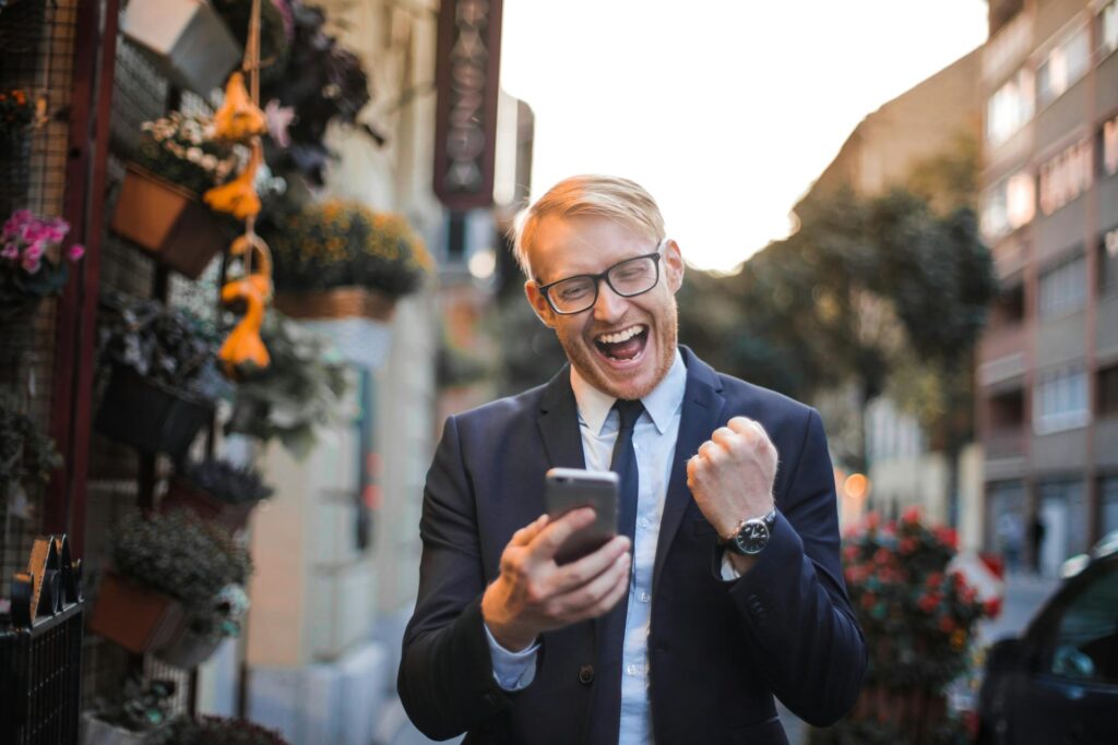 Joyful man celebrating success with smartphone outdoors.
