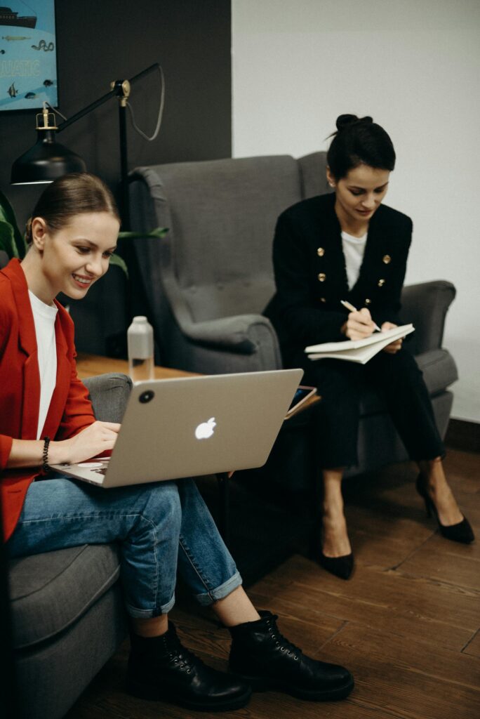 Two women working with laptop and notebook in office.