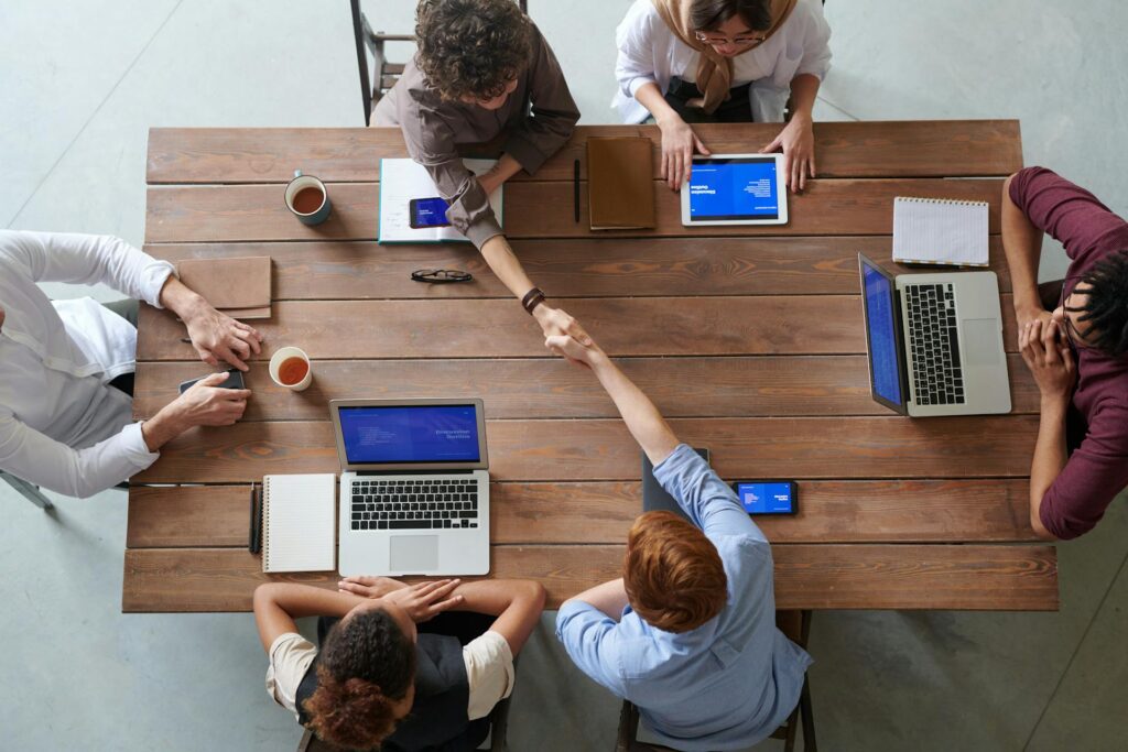 Top view of team meeting with handshake and laptops.