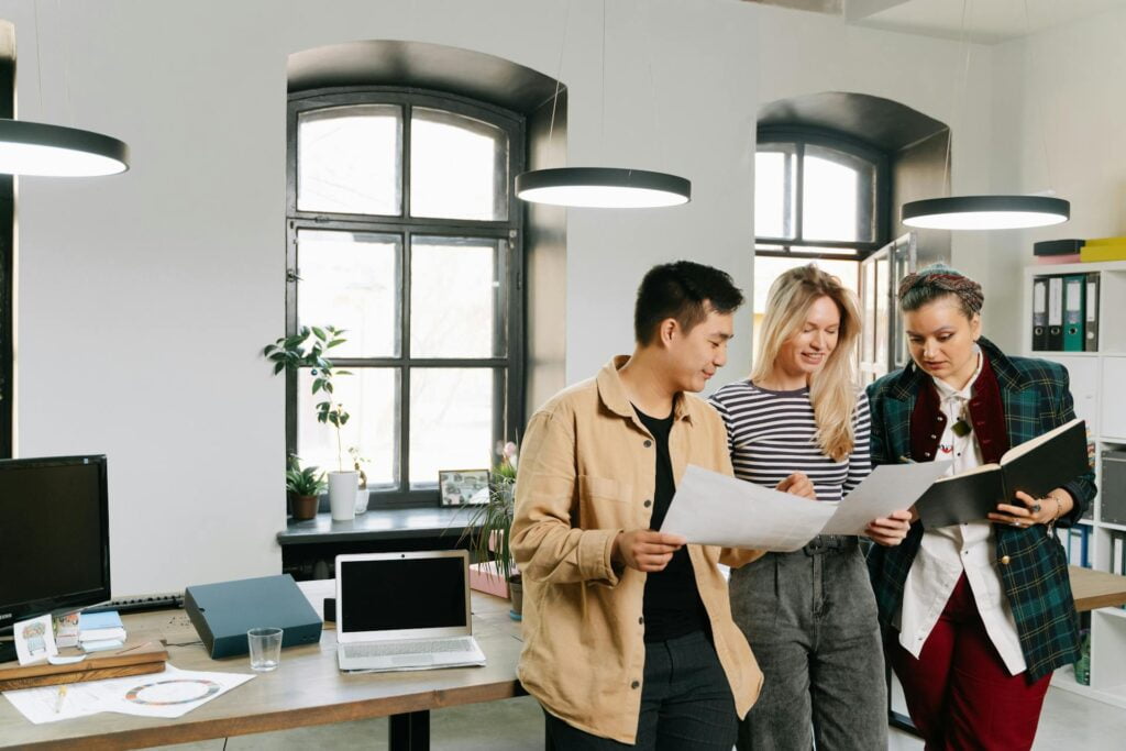 Three coworkers discussing documents in modern office.