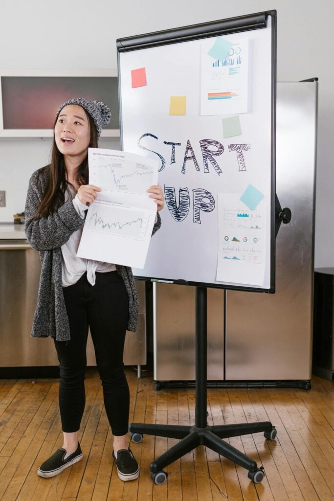 Woman presenting startup growth charts on whiteboard.