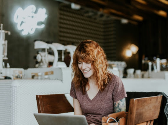 Woman smiling at laptop in cozy cafe setting.